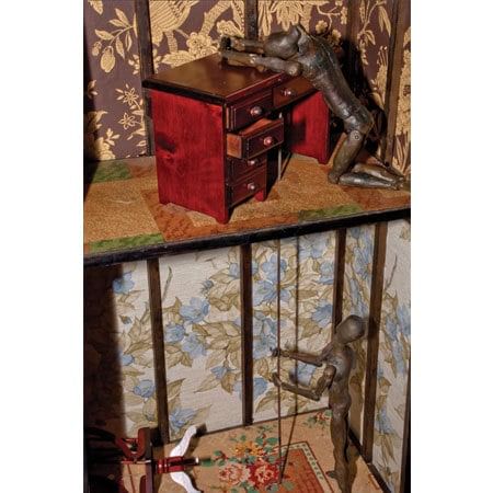 assemblage construction with one human form on top level and another below pulling on a string that goes up to the form on the top level