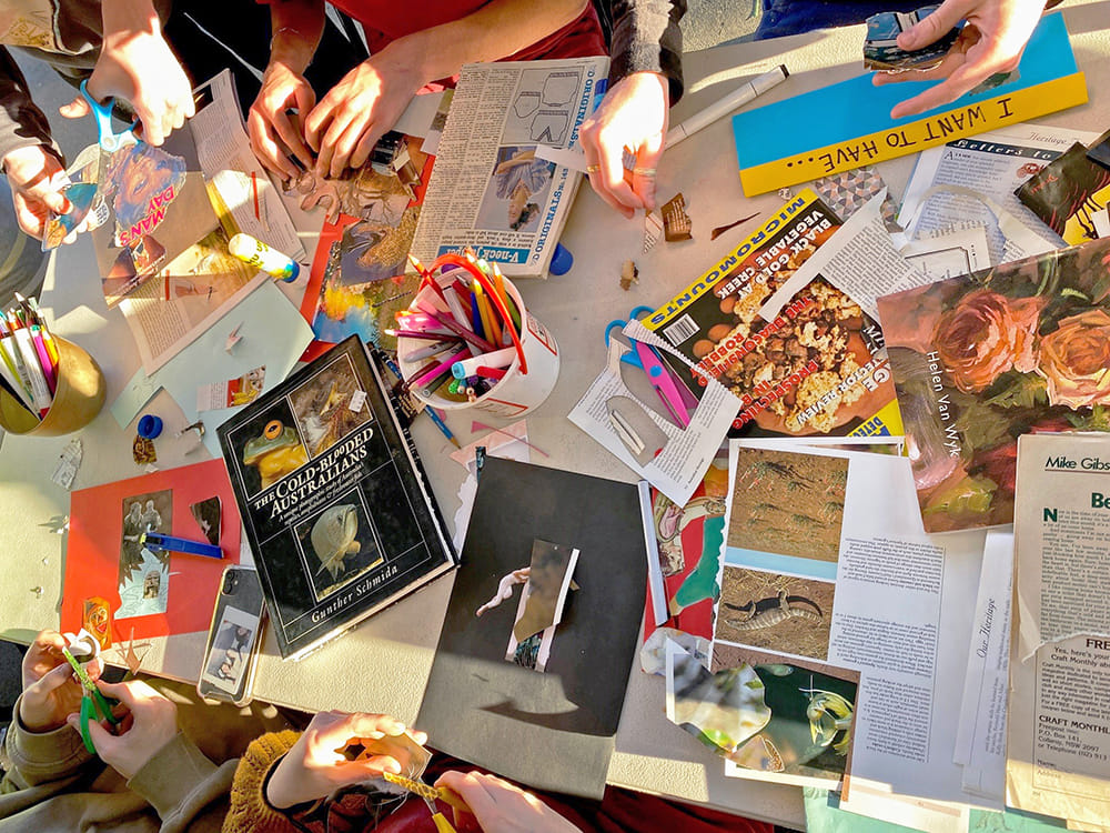 image of peoples hands working at table covered in collage materials 