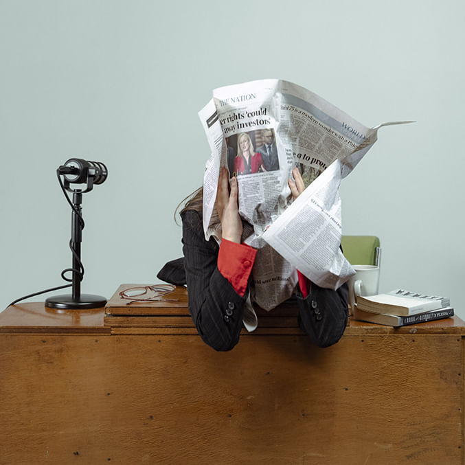person sitting at news desk with a page from a newspaper wrapped around their head