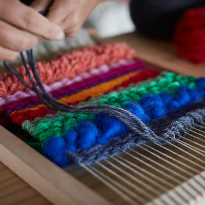 person using a weaving loom multicoloured fibres