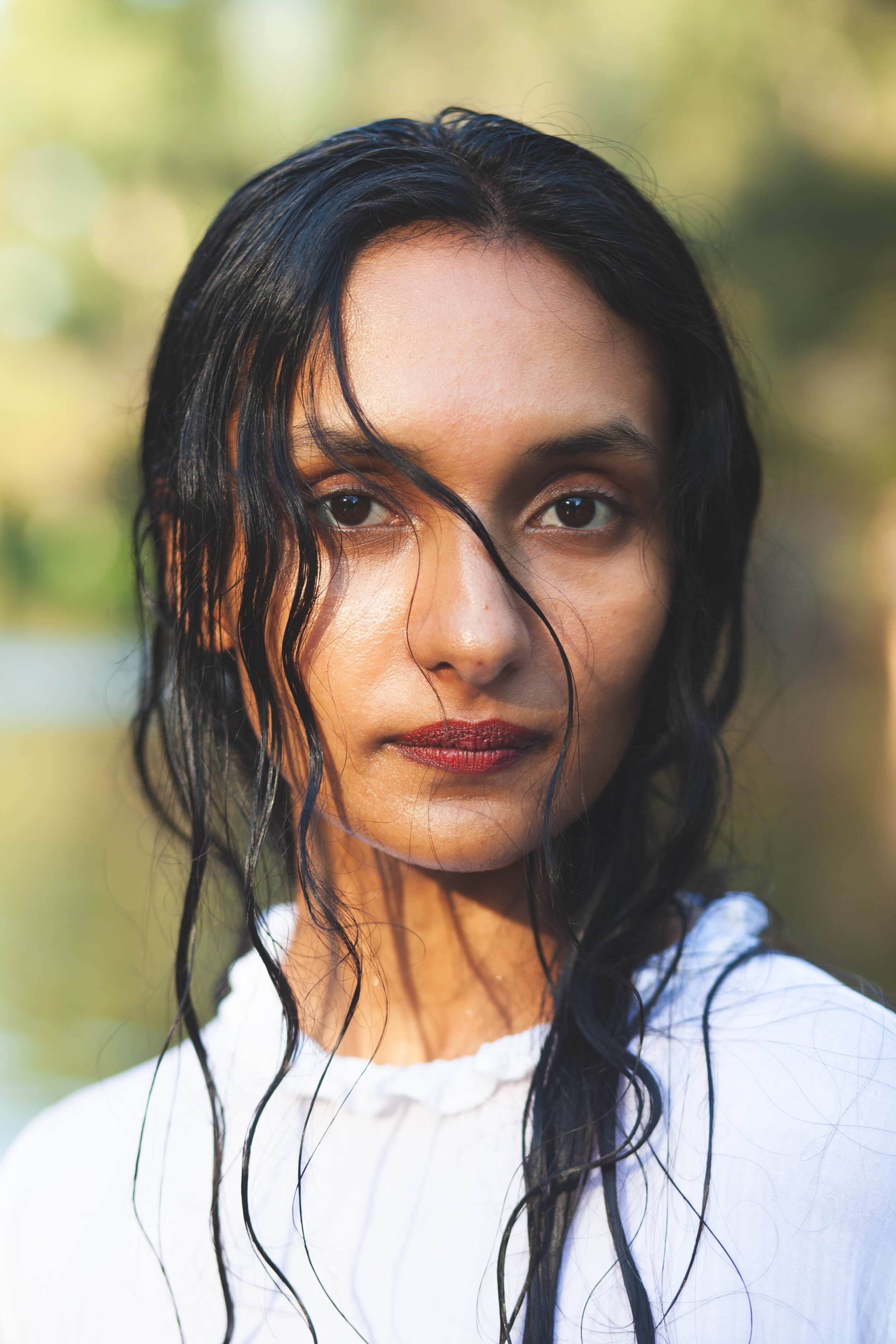 A close up portrait of a woman who is looking straight into the camera. She has long black hair, dark eyes and a white shirt. 