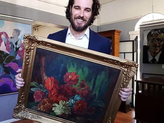 man holding still life painting of roses in a silver frame