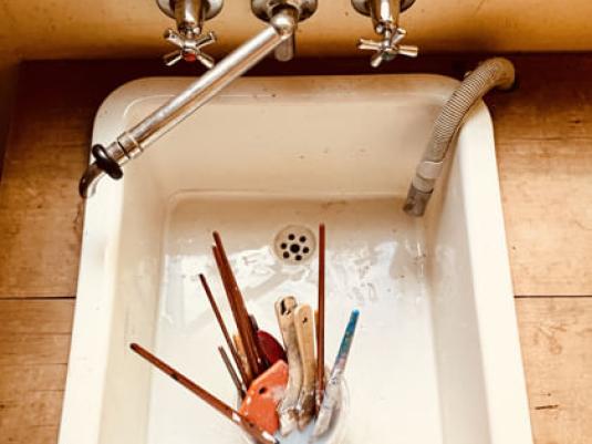a sink with a container holding multiple paint brushed and other painting tools