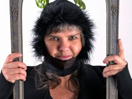 photo of Karla Dickens in hat with leaves for ears holding ornate frame framing her face