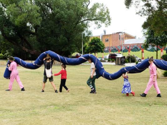 people carrying a large snake sculpture through to park