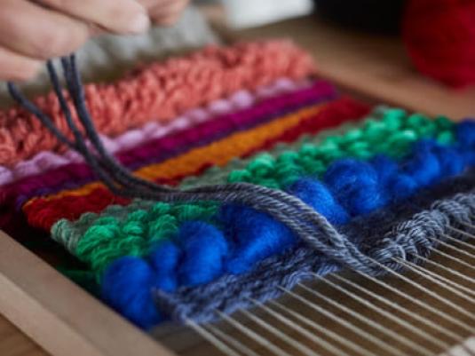 person using a weaving loom multicoloured fibres