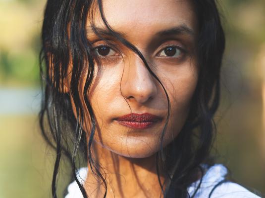 A close up portrait of a woman who is looking straight into the camera. She has long black hair, dark eyes and a white shirt.