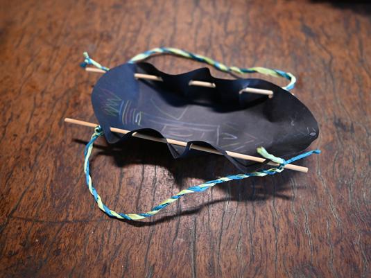 A photo of a handmade treasure carrier artwork. It is made from black carboard, string and wood.