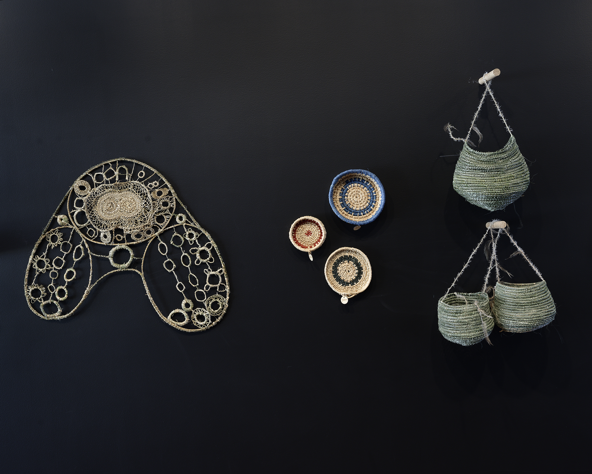 Aboriginal woven objects mounted on a black wal.. They are various shspaes, patterns, and sizes