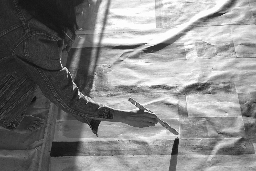 A black and white photo of the artist painting a canvas on the ground
