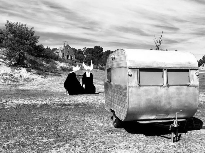 A black and white photo of a vintage caravan with two nuns in the background