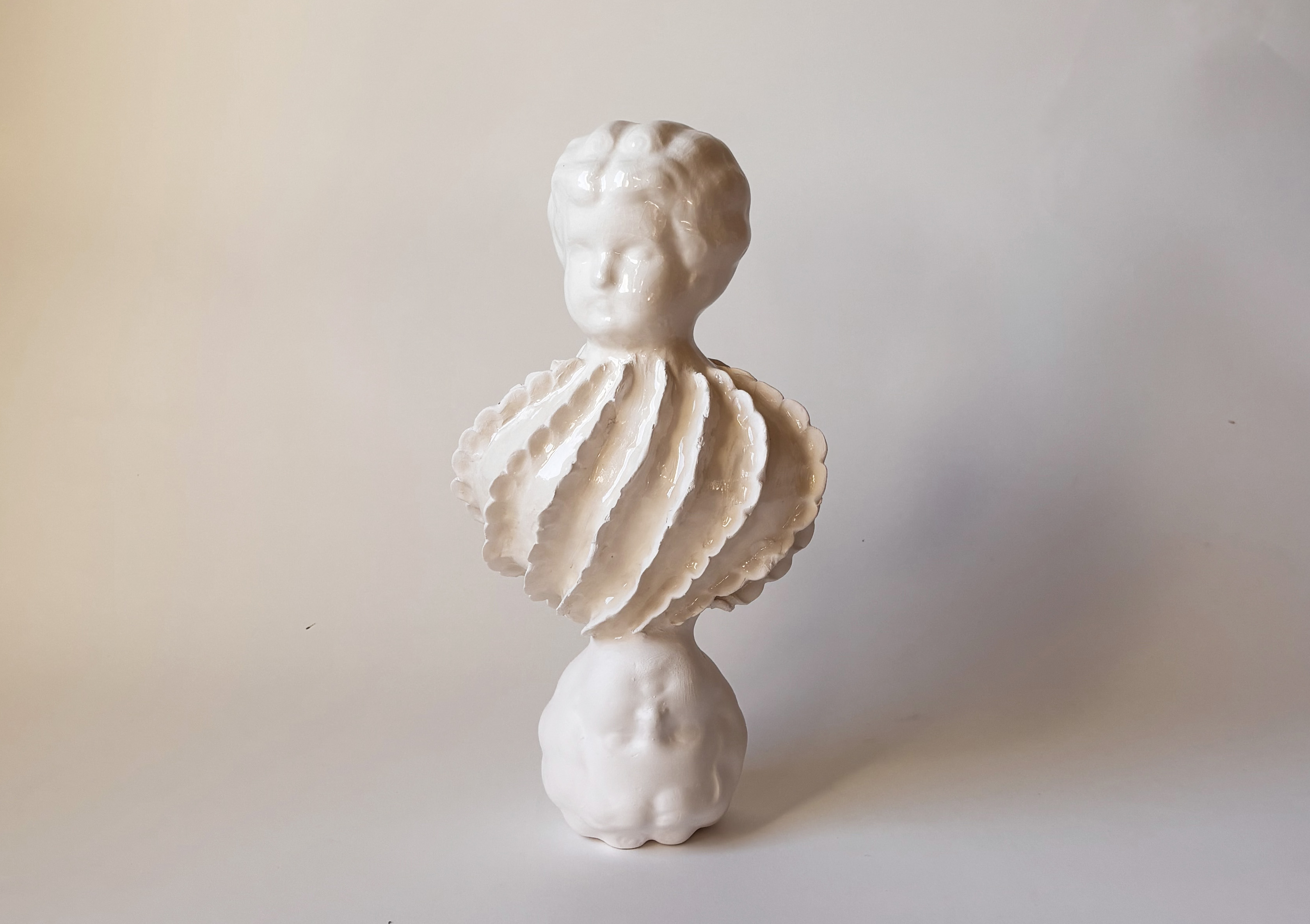 A white ceramic sculpture of two doll heads and a mollusc shape in between