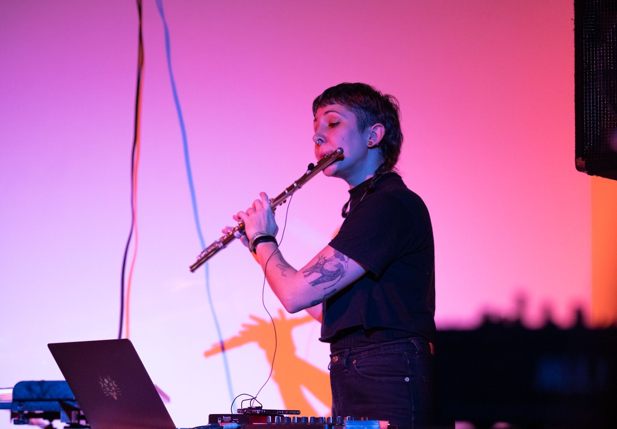 A non-binary person playing the flute, wearing black, with pink stage lighting