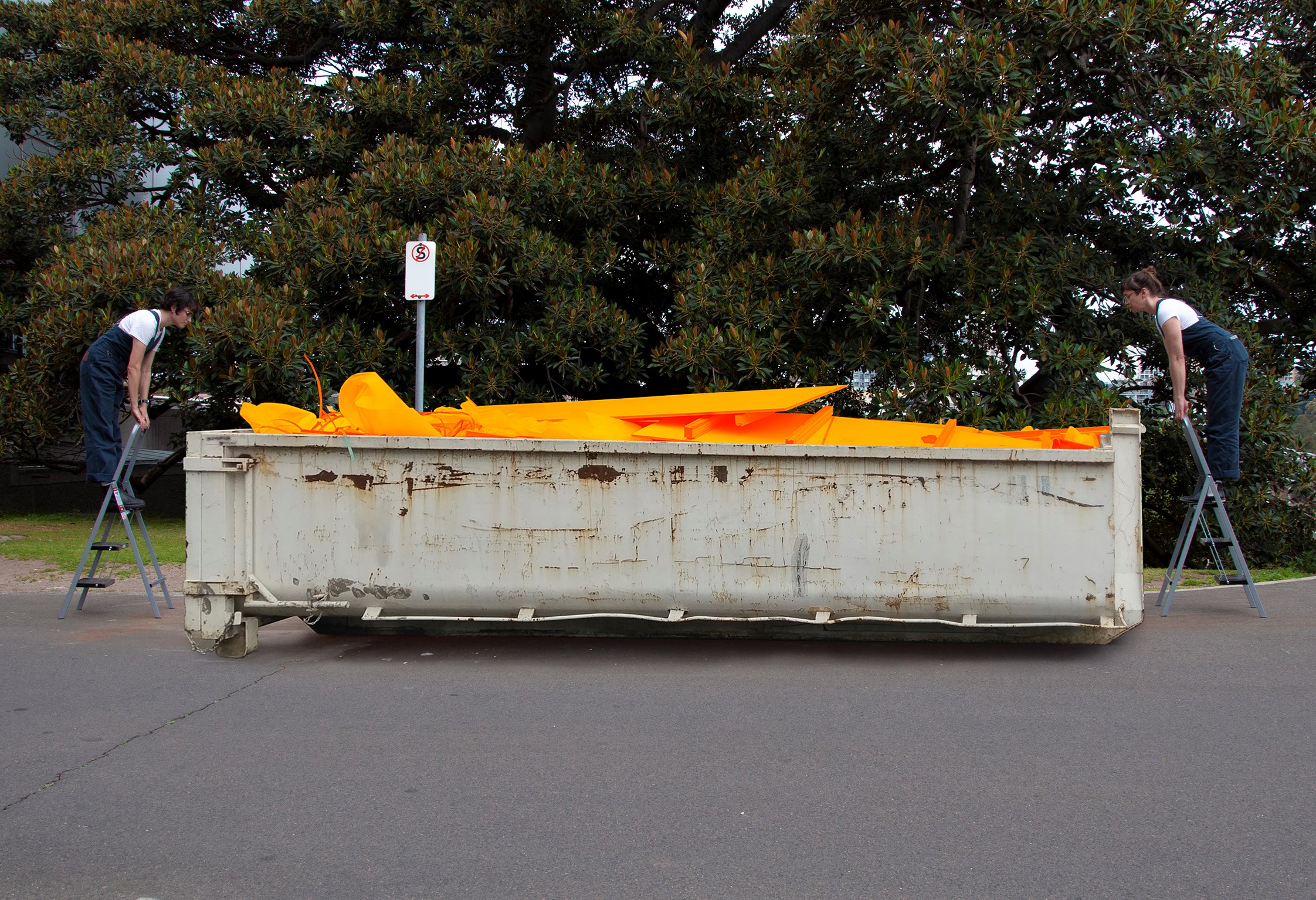 two people on ladders looking into a full skip bin