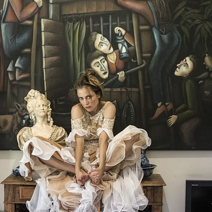 young woman in frilly dress with paintings of puppets behind her and a statue of woman beside her