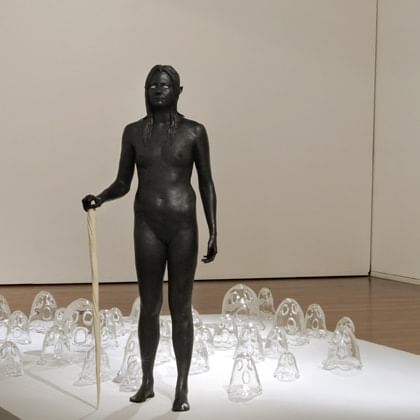 Bronze statue of woman standing in front of hand blown clear class ghost sculptures
