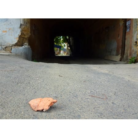stone in foreground of photo with an archway showing light at end of tunnel in background