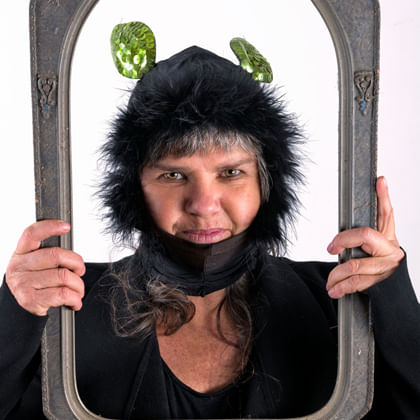 photo of Karla Dickens in hat with leaves for ears holding ornate frame framing her face