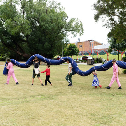people carrying a large snake sculpture through to park