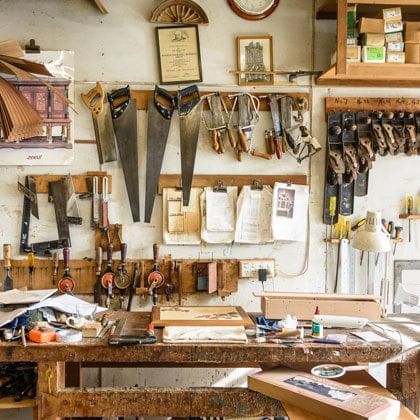 woodworking tools in workshop including saws, hand drills, chisels, planes, squares, design drawings, shelves and workbench 