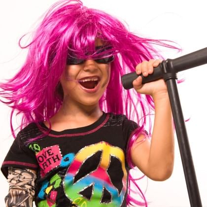 child in pink wig and sunglasses rocking out with microphone in hand 