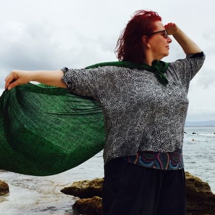 woman looking out to sea with holding a green cape with a rock and sea behind her 