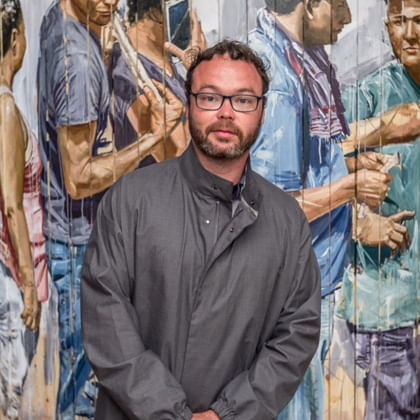 artist Fintan Magee standing in front of is mural of a group of people. 