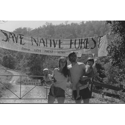 Nan and Hugh Nicholson with their two children on a dirt road with a 'save native forest' banner behind them 