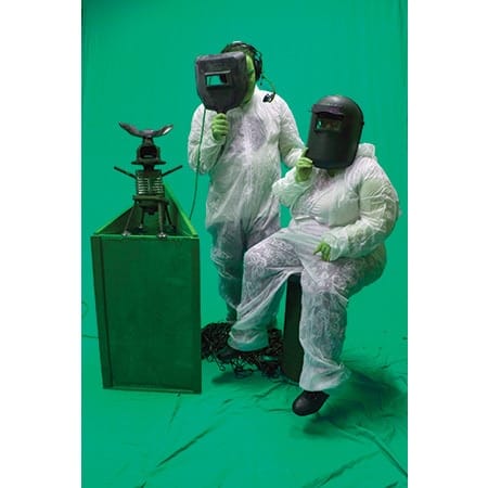 two people in safety suits wearing welding goggle looking at a contraption in front of them 