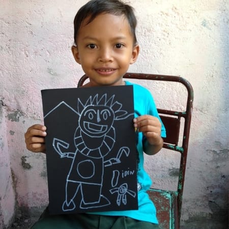a child on a chair showing the viewer their artwork