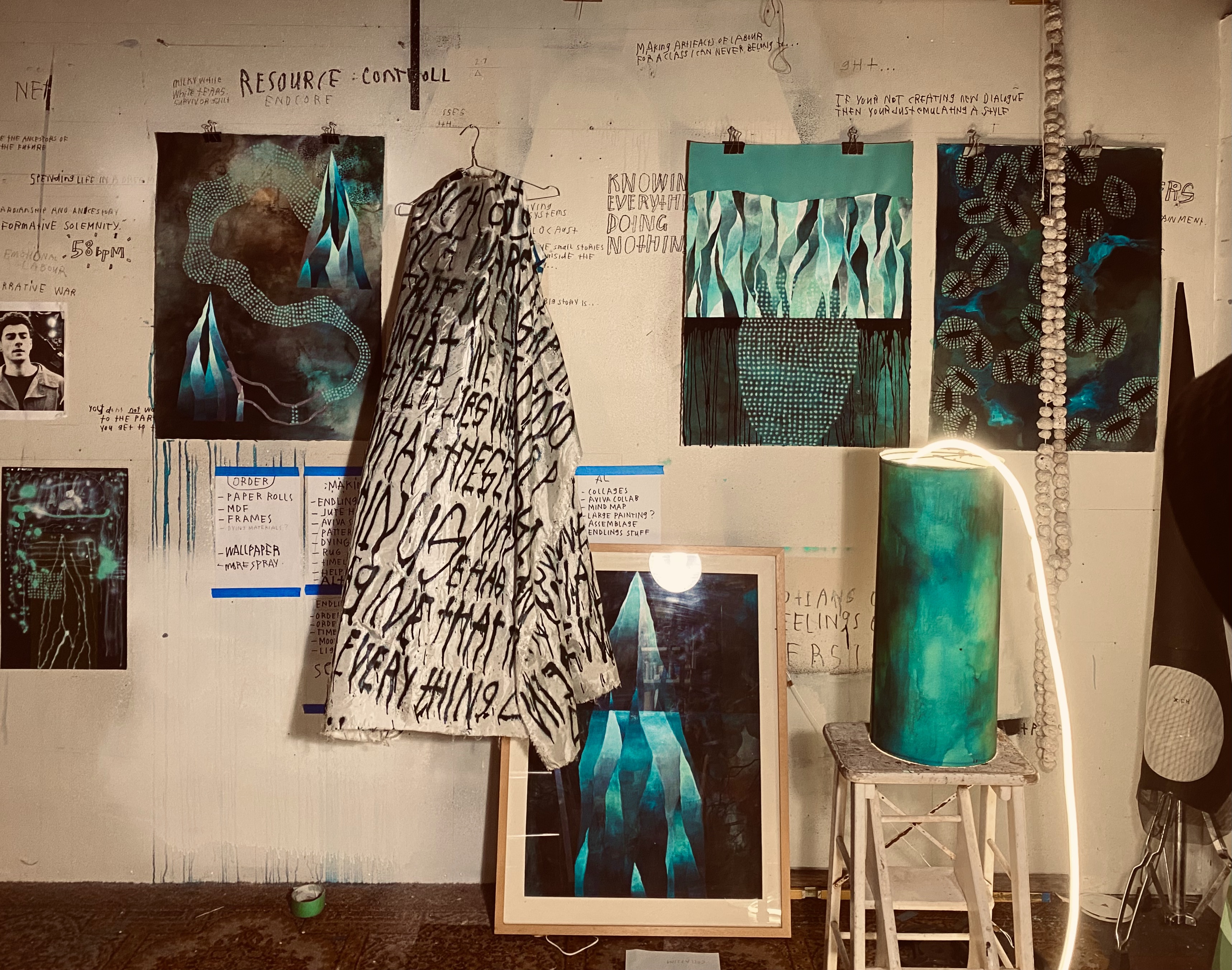 An artist studio with a variety of creative outputs - collage, costume, notes. The colours are white, back and green. 