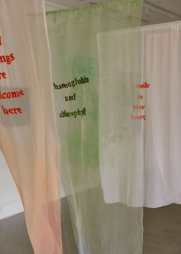3 banners of sheer material with words embroidered on them. The colours are orange and green. 