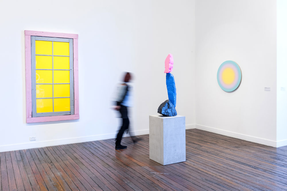 person walking past pink, blue and pink sculpture of a mountain