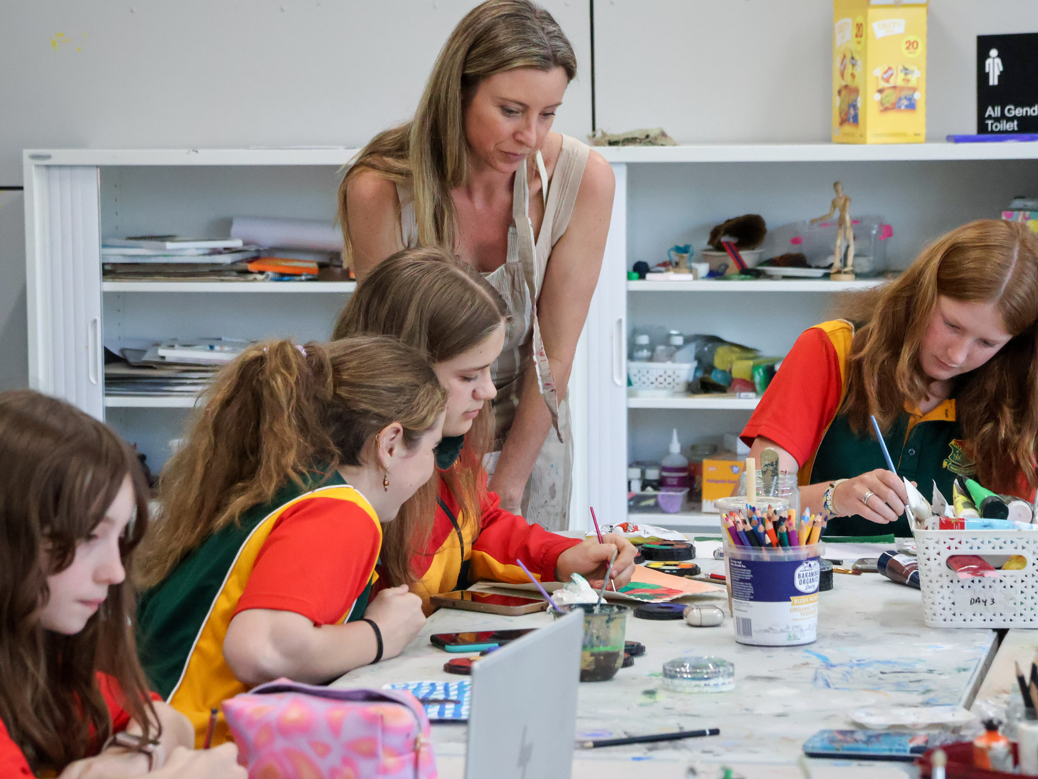 4 female highschool students at a table making art, with their female teacher assisting them
