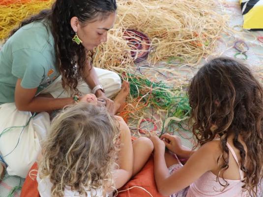 Kyra Togo sitting with children using fibre to weave colourful handmade objects