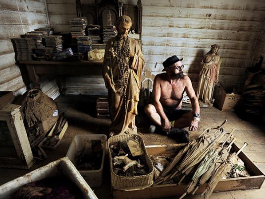 A man sitting on the floor of his flooded house surrounded by mud covered walls and objects