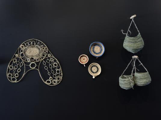 Aboriginal woven objects mounted on a black wal.. They are various shspaes, patterns, and sizes