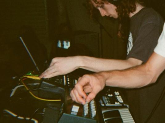A young man with long red curly hair, wearing headphones and playing electronic music