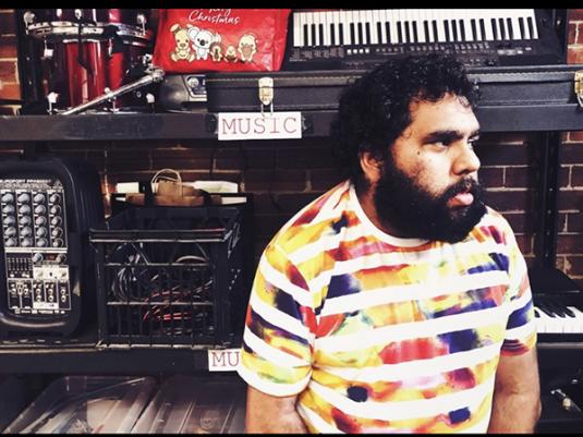 A First Nations man sitting in his music studio surrounded by equipment