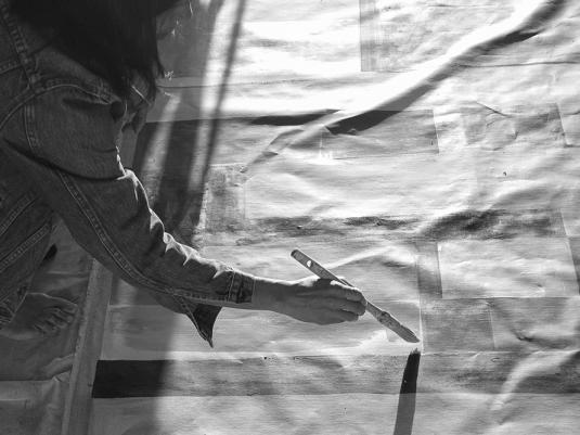 A black and white photo of the artist painting a canvas on the ground
