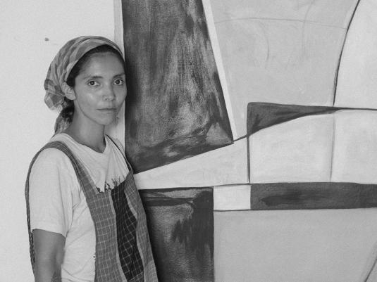 A woman of colour standing in front of her large scale painting