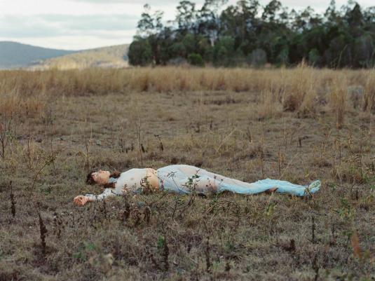 A woman wearing light blue lying down in a field of dry grass