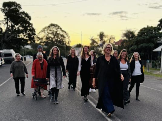 A group of older women walking down the street with the sunset behind them