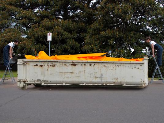 two people on ladders looking into a full skip bin