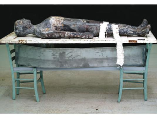 sculpture of body on recycled door, chairs and tin coffin liner