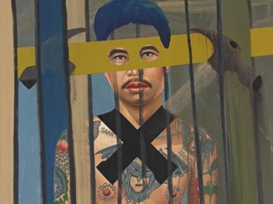 man behind bars with large black X across his tatooed chest