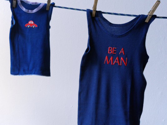 child's singlet with car motif  hanging on clothes line beside men's singlet with 'be a man' caption on front