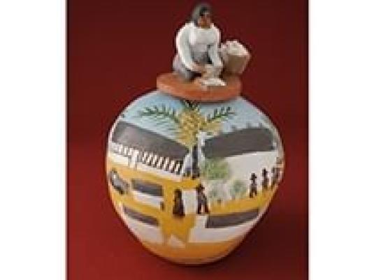 ceramic pot with detail of people and buildings and a woman sitting on top of the lid