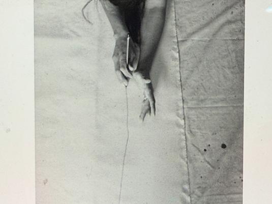 A black and white photo of a woman lying on a large sheet of canvas, marking it with a pencil