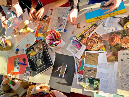 image of peoples hands working at table covered in collage materials